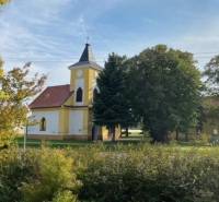 Práznovce – Spoluvlastnícky podiel na ornej pôde - Kostol obklopený zeleňou v Práznovciach na poľnohospodárskych a lesných pozemkoch.