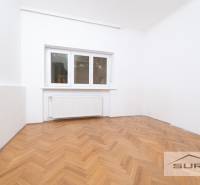 PRENÁJOM 4-IZBOVÉHO BYTU | ZÁHRADA | DVOJGARÁŽ | KRČMÉRYHO ULICA - Izba v 4-izbovom byte s bielymi stenami a podlahou s dreveným dekorom.