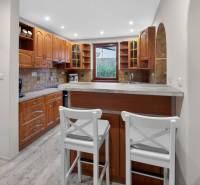 Rodinný dom s veľkým pozemkom a priestorom na podnikanie – T.Jastrabie - Kuchyňa v rodinnom dome s barovým pultom, drevenými skrinkami a podlahou s dreveným dekorom.