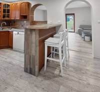 Rodinný dom s veľkým pozemkom a priestorom na podnikanie – T.Jastrabie - Kuchyňa v rodinnom dome s barovým pultom, bielymi stoličkami a podlahou s dreveným dekorom.