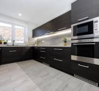 NOVOSTAVBA BUNGALOVU S MNOŽSTVOM PRIESTORU, v slepej ulici, Pružina - Kuchyňa v rodinnom dome s tmavým nábytkom a podlahou s dreveným dekorom.