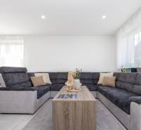 NOVOSTAVBA BUNGALOVU S MNOŽSTVOM PRIESTORU, v slepej ulici, Pružina - Obývačka v rodinnom dome s veľkou sedacou súpravou a kvetmi na stolíku.