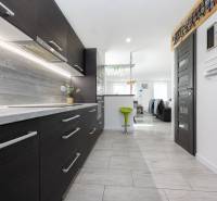 NOVOSTAVBA BUNGALOVU S MNOŽSTVOM PRIESTORU, v slepej ulici, Pružina - Interiér rodinného domu s modernou kuchyňou, barovou stoličkou a podlahou s dreveným dekorom.