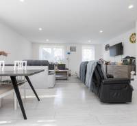 NOVOSTAVBA BUNGALOVU S MNOŽSTVOM PRIESTORU, v slepej ulici, Pružina - Priestranná obývacia izba s podlahou s dreveným dekorom, sedačkou a krbom v rodinnom dome.