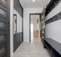 NOVOSTAVBA BUNGALOVU S MNOŽSTVOM PRIESTORU, v slepej ulici, Pružina - Chodba v rodinnom dome s tmavými dverami, vešiakom a skrinkou.