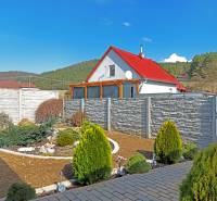 NOVOSTAVBA BUNGALOVU S MNOŽSTVOM PRIESTORU, v slepej ulici, Pružina - Rodinný dom v Pružine s červenou strechou, záhradou a kamenným plotom.