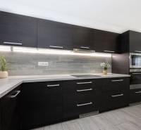 NOVOSTAVBA BUNGALOVU S MNOŽSTVOM PRIESTORU, v slepej ulici, Pružina - Tmavá kuchyňa s dekorom dreva a vstavanými spotrebičmi v rodinnom dome.