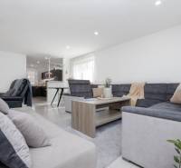 NOVOSTAVBA BUNGALOVU S MNOŽSTVOM PRIESTORU, v slepej ulici, Pružina - Obývacia izba v rodinnom dome s podlahou s dreveným dekorom a veľkým rohovým gaučom.