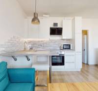 Pekný 2-izbový byt s lodžiou | investičná príležitosť | - Kuchynský kút v 2-izbovom byte s bielymi skrinkami a podlahou s dreveným dekorom.