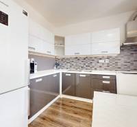 | Priestranný 2,5-izb. byt s walk-in šatníkom | parkovanie | - Kuchyňa v 2-izbovom byte s bielymi skrinkami a podlahou s dreveným dekorom.