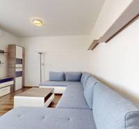 | Priestranný 2,5-izb. byt s walk-in šatníkom | parkovanie | - Obývačka s modrou sedačkou, nástennými policami a podlahou s dreveným dekorom v 2-izbovom byte.