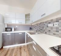 | Priestranný 2,5-izb. byt s walk-in šatníkom | parkovanie | - Kuchynská linka v 2-izbovom byte s bielou chladničkou a podlahou s dreveným dekorom.