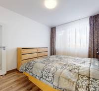 | Priestranný 2,5-izb. byt s walk-in šatníkom | parkovanie | - Svetlá spálňa s podlahou s dreveným dekorom a posteľou v 2-izbovom byte.