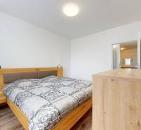 | Priestranný 2,5-izb. byt s walk-in šatníkom | parkovanie | - Spálňa so štýlovou posteľou a podlahou s dreveným dekorom v 2-izbovom byte.