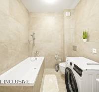 Na prenájom 2-izb. byt s terasou, Dun. Streda -Florida - Kúpeľňa so svetlými obkladmi, vaňou, práčkou a dekoratívnymi rastlinami v 4-izbovom byte.