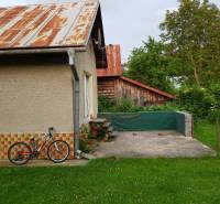 PREDAJ – Rodinný dom s druhou samostatnou stavbou, garážou  - Rodinný dom v Blatnici so záhradou, bicykel opretý o stenu, viditeľný drevený prístrešok.