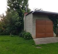 PREDAJ – Rodinný dom s druhou samostatnou stavbou, garážou  - Garáž v rodinnom dome na ulici v Blatnici, obklopená zeleňou a popínavými rastlinami.