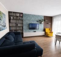 Predaj 3-izbový byt s terasou 20m2, parkovanie, Dunajská Lužná - Obývačka s modrou sedačkou, žltým kreslom a podlahou s dreveným dekorom v 3-izbovom byte.