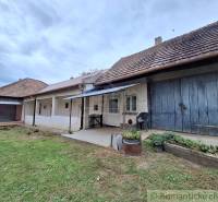 Pôvodný päťizbový rodinný dom s hospodárskymi budovami blízko centra o - Rodinný dom v Mužli s tradičnou fasádou, verandou a bujnou záhradou.