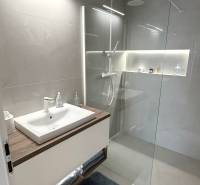 2 izbový A.3.1.- 58,91 m2 Bell Residence  - Kúpeľňa s umývadlom, skleneným sprchovým kútom a svetlými dlaždicami v 2-izbovom byte.