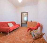 Na predaj rodinný dom Trnava, Zelenečská ulica, pozemok 1085 m2 - Obývacia izba s červeným gaučom, kreslom, časopismi a podlahou s dreveným dekorom v rodinnom dome.