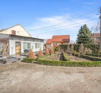 Komerčný objekt s pozemkom – možnosť zmeny na rodinný dom - Obchodné priestory v Okoči s úpravou záhrady, obklopené stromami a kríkmi.