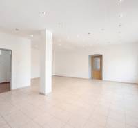 Komerčný objekt s pozemkom – možnosť zmeny na rodinný dom - Priestranné obchodné priestory s bielymi stenami, dlažbou a rozsvietenými stropnými svetlami.