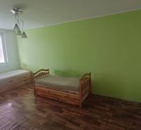 Na predaj 2i byt Levice - Interiér 2-izbového bytu s dvomi posteľami, podlaha s dreveným dekorom, zelená stena.
