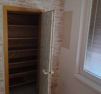 Na predaj 2i byt Levice - Skrinka s policami vedľa okna v 2-izbovom byte, priestor s imitáciou tehlovej steny.