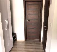 Na predaj apartmán s veľkou terasou Podhájská. - Garsónka s podlahou s dreveným dekorom, tmavými dverami a bielou skriňou.
