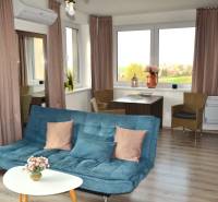 Na predaj veľký 49m2 apartmán Podhájská.  - Obývacia izba so sedačkou, stolíkom, rastlinami a podlahou s dreveným dekorom v 2-izbovom byte.
