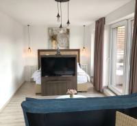 Na predaj štyri apartmány na jednom poschodí Podhájská - Obývacia izba v 2-izbovom byte s podlahou s dreveným dekorom a oddelenou spálňovou zónou.