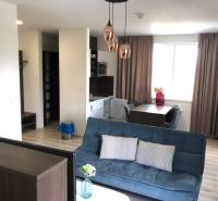 Na predaj štyri apartmány na jednom poschodí Podhájská - Obývacia izba v 2-izbovom byte s pohovkou a jedálenským stolom; podlaha s dreveným dekorom.