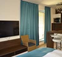 Na predaj štyri apartmány na jednom poschodí Podhájská - Garsónka s TV, dreveným nábytkom, kuchynským pultom a tyrkysovými závesmi.