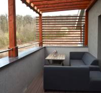 Na predaj štyri apartmány na jednom poschodí Podhájská - Balkón 2-izbového bytu s dreveným dekórom a výhľadom na zeleň.