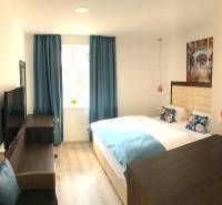 Na predaj štyri apartmány na jednom poschodí Podhájská - Svetlá izba v 2-izbovom byte s modrými závesmi a podlahou s dreveným dekorom.