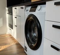 Exkluzívna ponuka moderného 1-izbového bytu s balkónom v meste Vráble - Kuchyňa v 1-izbovom byte so vstavanou práčkou a podlahou s dreveným dekorom.