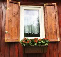 Bývanie v prírode, na dosah mesta, murov. chatka s celoročným využitím - Okno rodinného domu v Bohdanovciach nad Trnavou s okenicami a kvetináčom s červenými kvetmi.