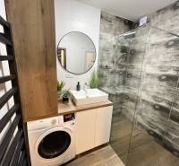 KOŠICE-2 IZBOVÝ BYT,NOVOSTAVBA,KOMPLET ZARIADENÝ,VL.PARK. MIESTO - Kúpeľňa so sprchovacím kútom, umývadlom, práčkou a podlahou s dreveným dekorom v 2-izbovom byte.