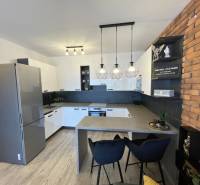 KOŠICE-2 IZBOVÝ BYT,NOVOSTAVBA,KOMPLET ZARIADENÝ,VL.PARK. MIESTO - Kuchyňa v 2-izbovom byte s podlahou s dreveným dekorom a tehlovým obkladom na stene.