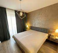 KOŠICE-2 IZBOVÝ BYT,NOVOSTAVBA,KOMPLET ZARIADENÝ,VL.PARK. MIESTO - Spálňa s posteľou, podlahou s dreveným dekorom a závesmi v 2-izbovom byte.