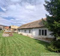 Vymeňte mestský hluk za ticho Bystričky: Domček s dušou a potenciálom - Rodinný dom v Ozdíne s pôvodným vzhľadom a trávnatým dvorom, obklopený stromami.