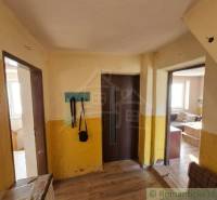 Vymeňte mestský hluk za ticho Bystričky: Domček s dušou a potenciálom - Interiér rodinného domu s podlahou s dreveným dekorom, žlté steny, vešiak, pohovka.