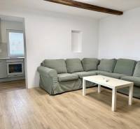 Na predaj 2 izbový murovaný domček, Bratislava, Záhorská Bystrica - Obývacia izba s rohovou pohovkou, podlahou s dreveným dekorom a kuchyňou v rodinnom dome.