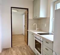 Na predaj 2 izbový murovaný domček, Bratislava, Záhorská Bystrica - Kuchyňa v 2-izbovom byte s podlahou s dreveným dekorom a bielymi skrinkami.