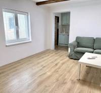 Na predaj 2 izbový murovaný domček, Bratislava, Záhorská Bystrica - Obývačka v rodinnom dome s pohovkou, stolom a podlahou s dreveným dekorom.