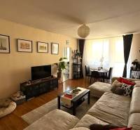 Pekný zariadený 3 izbový byt s lodžiou, Púpavová ulica, BA.Karlova Ves - Obývacia izba 3-izbového bytu s pohovkou, televízorom a jedálenským stolom, podlaha s dreveným dekorom.