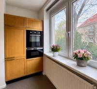Tichý 2i byt v TOP Lokalite Nív | Trenčianska, BA - Kuchyňa v 2-izbovom byte s dreveným dekorom a veľkými oknami.