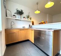 Tichý 2i byt v TOP Lokalite Nív | Trenčianska, BA - Kuchyňa v 2-izbovom byte, sivé dlaždice, drevené skrinky, závesné svetlá, rastliny na poličke.