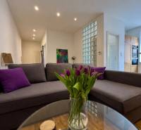 Tichý 2i byt v TOP Lokalite Nív | Trenčianska, BA - Obývačka v 2-izbovom byte s pohovkou a skleneným stolom s tulipánmi.